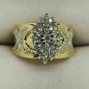 Puede incluir: Un anillo de oro amarillo que presenta un grupo en forma de marquesa de numerosas piedras pequeñas, redondas y transparentes en el centro. La banda ancha está hecha de oro amarillo y está decorada con piedras pequeñas, redondas y transparentes.