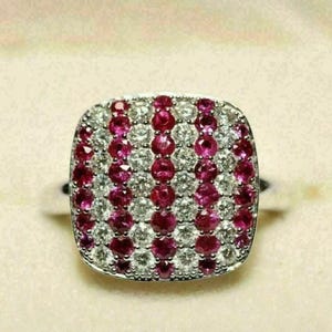 May include: A square-shaped ring featuring alternating vertical rows of round-cut red rubies and clear white diamonds. The stones are set in a metallic band, creating a dense, multi-stone cluster design that covers the entire top surface of the ring.