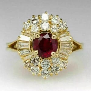 Può includere: Un anello in oro con un rubino centrale rosso intenso a taglio rotondo, circondato da un alone di diamanti bianchi a taglio baguette e rotondo. Le pietre sono disposte a grappolo su una fascia in oro giallo lucido dal design affusolato.