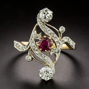 Puede incluir: Un anillo antiguo con un rubí ovalado central, rodeado por un diseño de filigrana dorada y adornado con numerosos diamantes pequeños. El anillo tiene una apariencia delicada y ornamentada, con una estética vintage. Los diamantes brillan sobre el fondo oscuro.