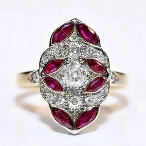 Könnte beinhalten: Ein Goldring mit einer länglichen, marquiseförmigen Cluster-Fassung. Die Mitte ist mit einem runden Diamanten im Brillantschliff verziert, umgeben von sechs marquiseförmigen roten Rubinen und mehreren kleinen runden Diamanten in Pavé-Fassung.
