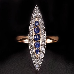 Peut inclure: Une bague en forme de marquise présentant une rangée verticale centrale de cinq saphirs bleu foncé sertis dans de l'or rose, entourée d'une bordure de petits diamants ronds transparents sertis dans de l'argent sur un anneau en or rose.