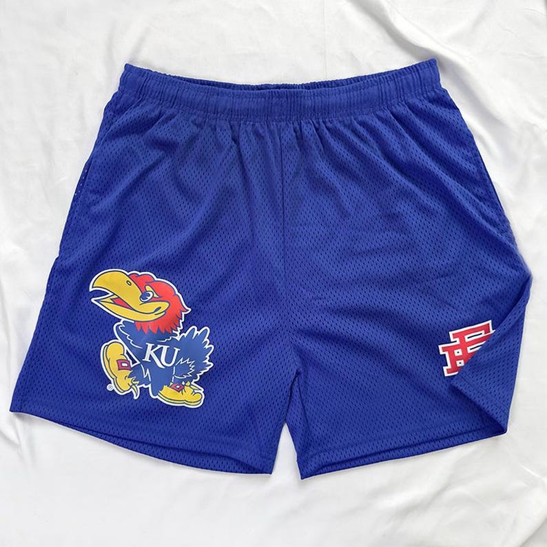 May include: Blue mesh shorts with a cartoon Jayhawk mascot graphic and the letters "KU", plus a red "F" logo. The shorts have an elasticated waistband and are made of breathable, athletic material.