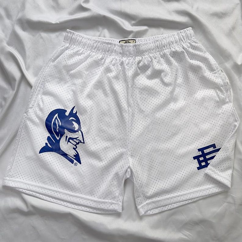 May include: White mesh shorts featuring a blue devil logo and a blue stylized letter logo. The shorts have an elasticated waistband. The shorts are designed for sports.