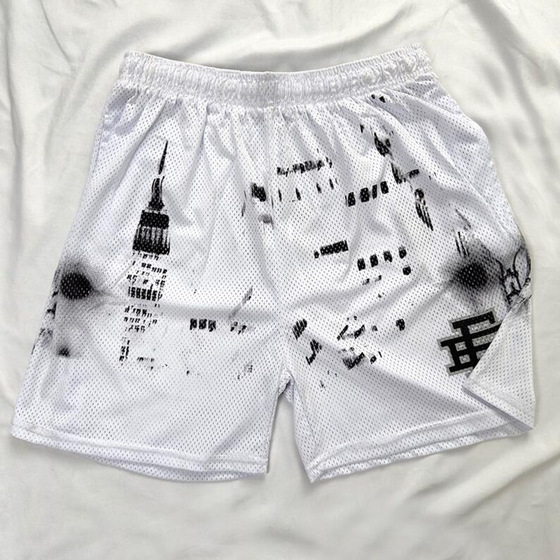 May include: White mesh athletic shorts with a black graphic print. The shorts have an elasticated waistband and a black logo on the lower right leg. The graphic appears to be a stylized cityscape.