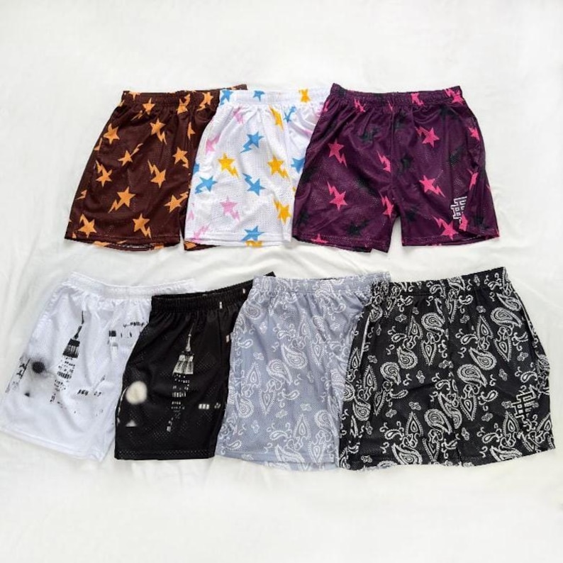 May include: Selection of mesh shorts in diverse colours and patterns. Designs include star patterns, paisley, and cityscapes. Colours include brown, white, purple, black, and grey. The shorts are lightweight and appear to be made of a breathable material.