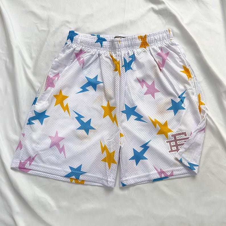 May include: White mesh shorts with an elasticated waistband, patterned with blue, yellow, and pink stars and lightning bolts. A small logo is on the right leg. Casual athletic wear.