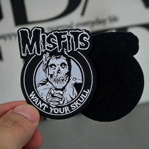 May include: Black and white embroidered patch featuring the word "Misfits" above a skull graphic. The phrase "Want Your Skull" is written around the skull. The patch has a black backing.