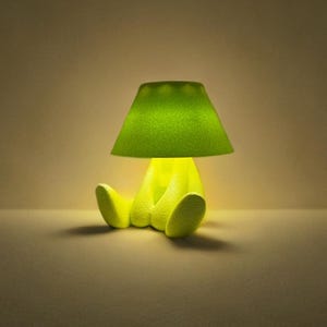 Könnte beinhalten: Eine skurrile, limettengrüne Lampe in Form einer sitzenden Figur. Die Lampe hat einen strukturierten Schirm und Sockel, wobei das Licht von innen kommt. Das Design ist modern und verspielt, passend für ein Kinderzimmer oder einen kreativen Raum.