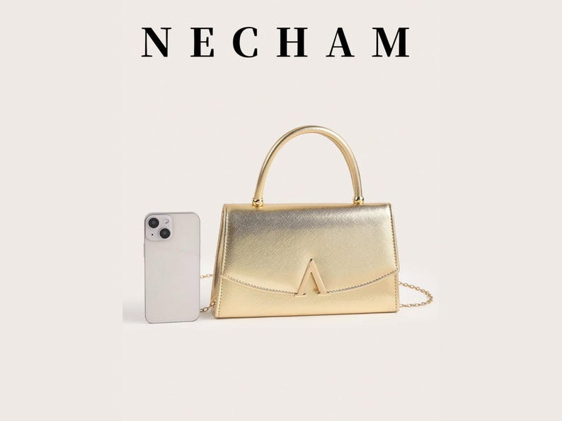 May include: A gold-colored handbag with a top handle and a chain strap. The bag has a rectangular shape with a flap closure and a gold-colored metal accent in the shape of a triangle. A smartphone is next to the bag. The word "NECHAM" is at the top.