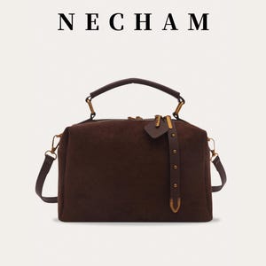 Puede incluir: Un bolso marr&oacute;n con asa superior y bandolera extra&iacute;ble. El bolso tiene forma rectangular con cierre de cremallera y herrajes dorados. La marca "NECHAM" se muestra encima del bolso.