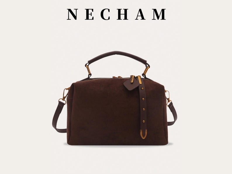 Puede incluir: Un bolso marr&oacute;n con asa superior y bandolera extra&iacute;ble. El bolso tiene forma rectangular con cierre de cremallera y herrajes dorados. La marca "NECHAM" se muestra encima del bolso.