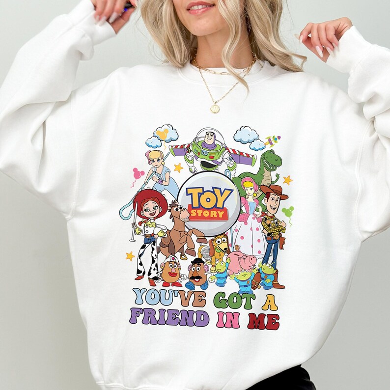 May include: White sweatshirt with a vibrant Toy Story character design, including Woody, Buzz Lightyear, and Jessie. The text "TOY STORY" is in a circle, and the phrase "YOU'VE GOT A FRIEND IN ME" is below the characters.