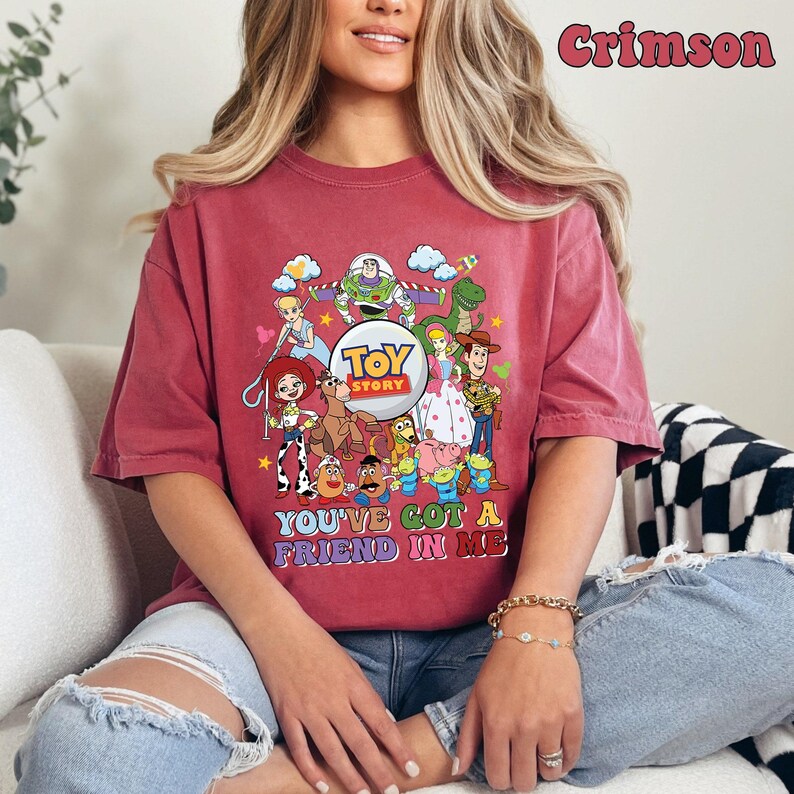 May include: Crimson t-shirt with a vibrant Toy Story character graphic. The design showcases Buzz Lightyear, Woody, and other characters from the film, accompanied by the text "YOU'VE GOT A FRIEND IN ME".