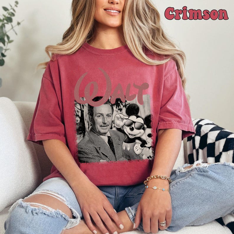 May include: A crimson short-sleeve t-shirt featuring a black and white graphic of Walt Disney and Mickey Mouse wearing sunglasses. The word Walt is printed in a large, stylized font above the graphic. The text Crimson appears in the top right.