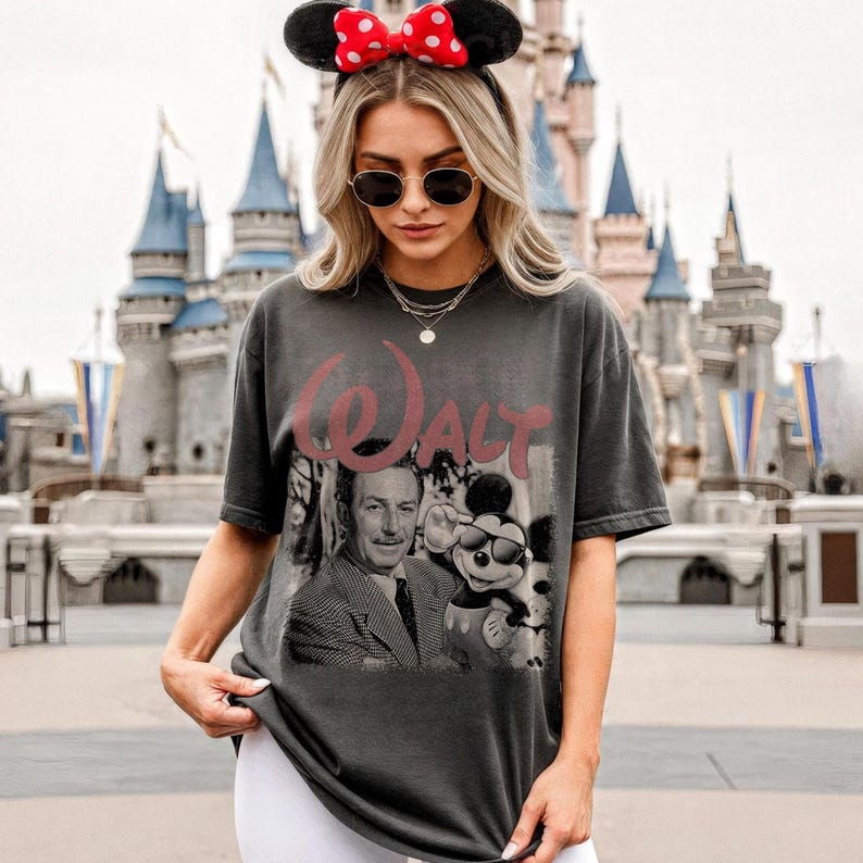 May include: A charcoal gray short-sleeve t-shirt featuring a faded graphic print of Walt Disney and Mickey Mouse. The text "Walt" is printed in a large, distressed red font above the black and white portrait of the two figures.