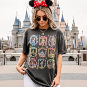 May include: A charcoal gray short-sleeve t-shirt featuring a grid of nine ornate frames containing illustrations of various animated characters and a central castle. The shirt is worn with black round sunglasses and a black headband with red polka-dot ears.