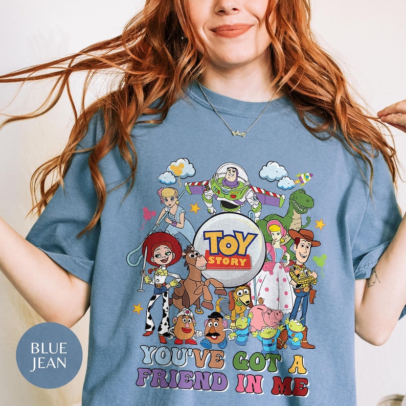 May include: Blue jean t-shirt with a vibrant Toy Story character graphic. The design showcases Buzz Lightyear, Woody, and other characters from the animated film. The text "TOY STORY" and "YOU'VE GOT A FRIEND IN ME" are also visible.