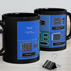 May include: Two black coffee mugs with a retro video game interface design. The design features a blue background with white text and pixelated graphics. One mug displays the text "GAME OVER" and "CONTINUE".