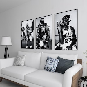 Puede incluir: Tres fotografías en blanco y negro enmarcadas de un jugador de baloncesto cuelgan sobre un sofá blanco con cojines decorativos. Las fotografías muestran al jugador en varias poses, incluida una con un cigarro y la palabra "Bulls" en su camiseta.