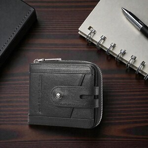 May include: Black leather wallet with a zipper closure and a snap closure. The wallet has a small logo on the front and is sitting on a wooden surface. A notebook and pen are in the background.