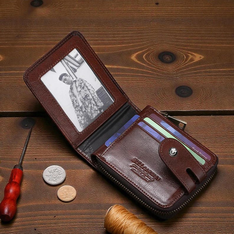 May include: Open brown leather wallet with a photo window, card slots, and a zippered compartment. The wallet is open, revealing a black and white photo. A small snap closure secures the card holder.