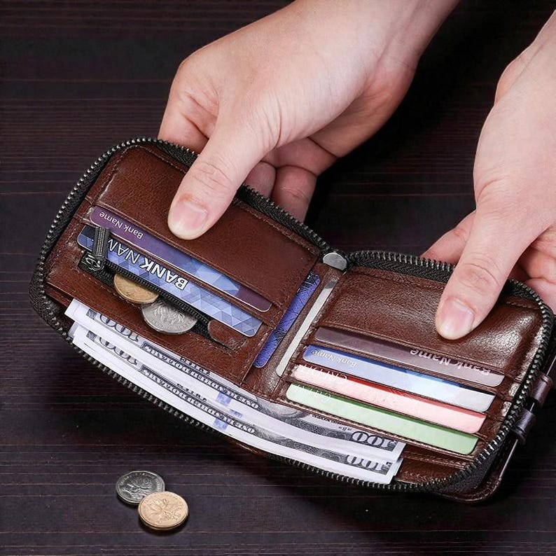 May include: Open brown leather wallet with a zipper closure, filled with cash, credit cards, and coins. The wallet is held open, showcasing its contents. The leather appears to be textured.