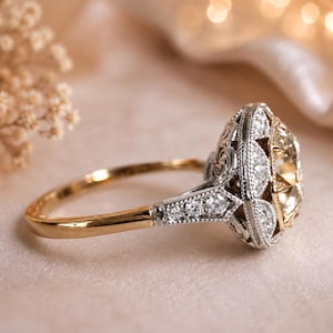 Peut inclure: Une bague de fiançailles bicolore avec une grosse pierre centrale claire. La bague a un anneau en or et un sertissage argenté détaillé autour de la pierre principale, orné de petits diamants. Le tout sur un fond rose clair.