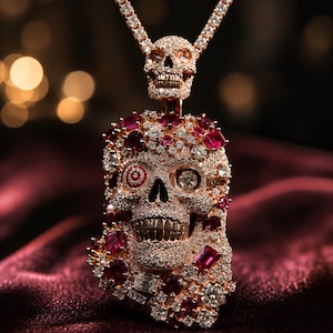 Puede incluir: Un collar con colgante de oro rosa con diseño de calavera incrustado con pequeñas piedras claras y gemas rojas más grandes. Una cuenca ocular contiene un símbolo de diana rojo y blanco. Un dije de calavera más pequeño cuelga de la cadena.