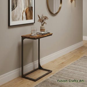 May include: A brown and black side table with a rectangular tabletop and a C-shaped metal frame. The tabletop has a wood grain pattern. The table is 24 inches long, 12 inches wide, and 24 inches high. The table is in a room with a painting and a mirror.