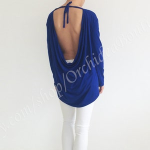 May include: A royal blue long-sleeved top with a low back and a draped design. The top is made of a soft, stretchy fabric.