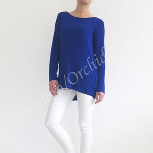 May include: A royal blue long-sleeved shirt with a high, round neckline. The shirt is made of a soft, stretchy fabric and has a slightly asymmetrical hemline.