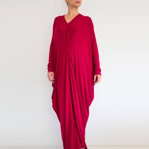 May include: A long-sleeved, deep red maxi dress with a V-neckline and a flowing, asymmetrical design.