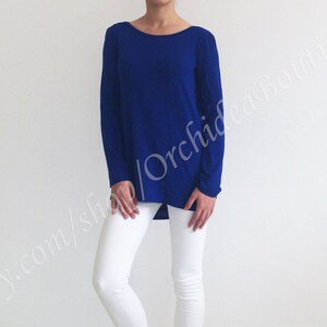 May include: A royal blue long-sleeved shirt with a relaxed fit and a slightly high neckline. The shirt is made of a soft, stretchy fabric and has a slightly longer length in the back.