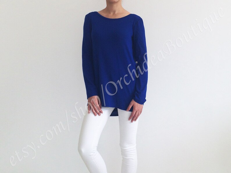 May include: A royal blue long-sleeved shirt with a relaxed fit and a slightly high neckline. The shirt is made of a soft, stretchy fabric and has a slightly longer length in the back.