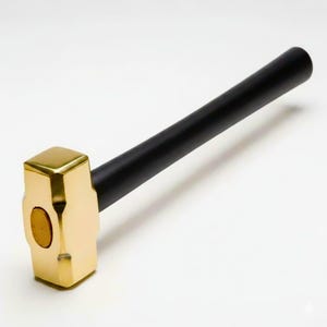 May include: A sledgehammer featuring a gold-coloured head and a black handle. The head is rectangular with a flat striking surface. The handle is cylindrical and appears to be made of wood or a similar material. The hammer is designed for heavy-duty tasks.