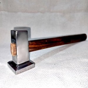 May include: A metal hammer with a polished, rectangular head and a dark wooden handle. The hammer head is silver and the handle is a rich brown color. The hammer is designed for woodworking or metalworking.