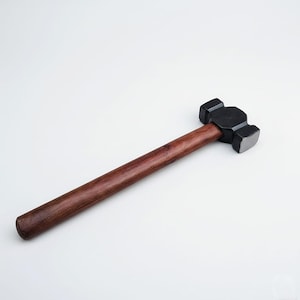 May include: A black and silver sledgehammer with a dark brown wooden handle. The hammer head is rectangular with a flat striking surface. The handle is long and cylindrical, made of polished wood.
