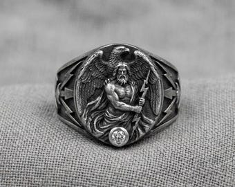 Anillo de sello de águila, banda de plata con relieve de rayo y piedra transparente.