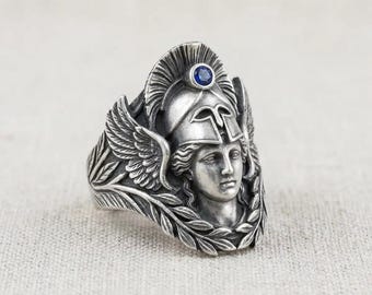 Anillo con forma de casco espartano, piedra azul plateada y laurel alado.
