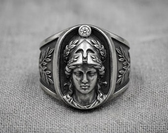 Anillo de plata de guerrero romano con casco y relieve de laurel y piedra transparente.