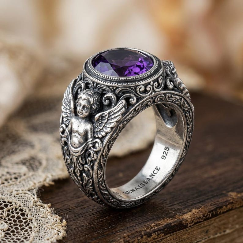 May include: A sterling silver Renaissance-style ring with a large oval, deep purple gemstone. The ring features detailed scrollwork, cherub figures with wings, and the inscription "RENAISSANCE 925".