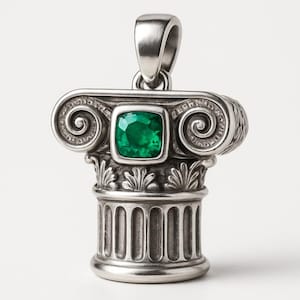 Op de afbeelding: Zilveren hanger in de vorm van een klassiek kolomkapiteel. De hanger heeft een vierkante, smaragdgroene edelsteen in het midden. Het ontwerp omvat ingewikkeld krulwerk en groeven, met een lus voor een ketting aan de bovenkant.