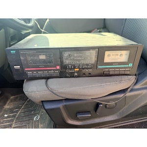 May include: A black MCS Series dual stereo cassette deck featuring two cassette compartments labeled 1 and 2, a central display panel with record level meters, various control buttons, input jacks, and a power switch on the front panel.