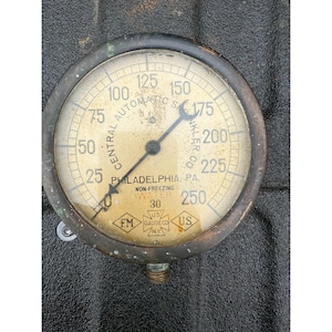 May include: An antique pressure gauge with a brass casing and a cream-colored face. The gauge reads up to 250, with markings for 25, 50, 75, 100, 125, 150, 175, 200, 225, and 250. The text "CENTRAL AUTOMATIC" and "PHILADELPHIA, PA." are visible.