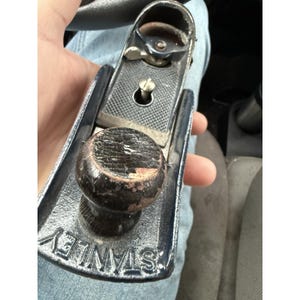 May include: A vintage Stanley hand plane, featuring a dark wooden knob and a textured metal body. The word "STANLEY" is embossed on the base. The tool shows signs of wear, indicating its age and use. This woodworking tool is designed for smoothing and shaping wood surfaces.