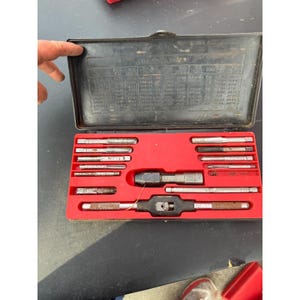 May include: A white ceramic mug with a black handle and the text "But First, Coffee" in a bold, black font. The mug is set against a blurred background, suggesting a cozy setting.