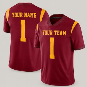 Op de afbeelding: Een bordeauxrood shirt met korte mouwen en gele accenten op de schouders. De voorkant toont de tekst YOUR TEAM boven het nummer 1 in het geel. De achterkant toont de tekst YOUR NAME boven het nummer 1 in het geel. Het shirt heeft een V-hals.