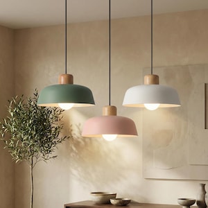 Puede incluir: Tres lámparas colgantes con un diseño minimalista. Cada lámpara presenta una pantalla redondeada de color verde, rosa y blanco, combinada con una parte superior de madera. Las lámparas cuelgan de cables negros, creando una estética moderna.