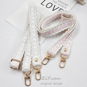 Op de afbeelding: Decoratieve tasriemen in wit en roze met goudkleurige hardware. Eén riem is wit met een kanten design, de andere is roze en wit. De riemen hebben goudkleurige sluitingen en zijn voorzien van het label "ZiYuan original design."